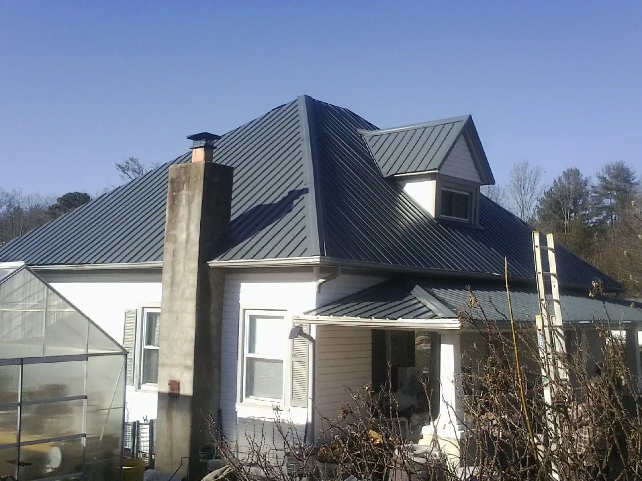 Dark blue standing seam metal roof on a white farmhouse with dormer — Slate & Tile Roof Repair by Roofing Brothers in Kentwood