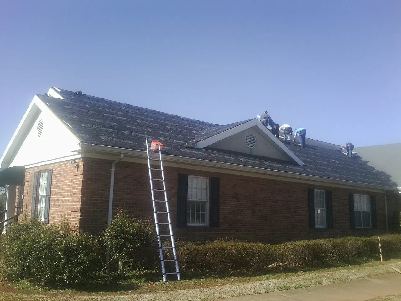 Crew tearing shingles off a brick ranch roof with a ladder set — Emergency Roof Repair work by our crew in Kentwood