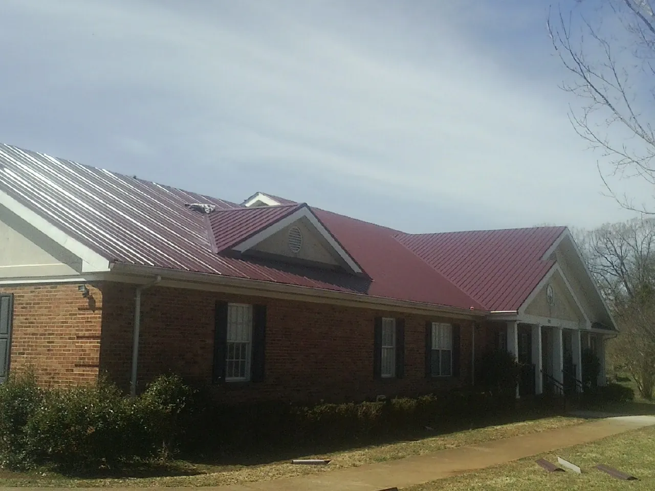 Red metal roof with gabled entries on a long brick building, from a Hail Damage Roof Repair job in Kentwood