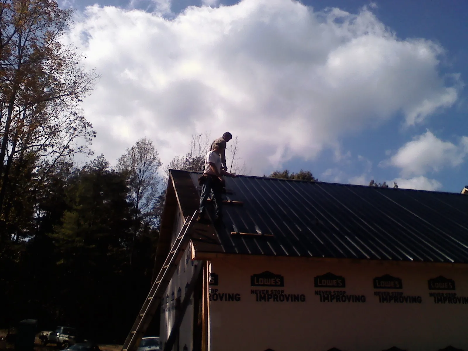 Roofer fastening dark metal panels high against a cloudy sky, from a Roof Inspection job in Kentwood
