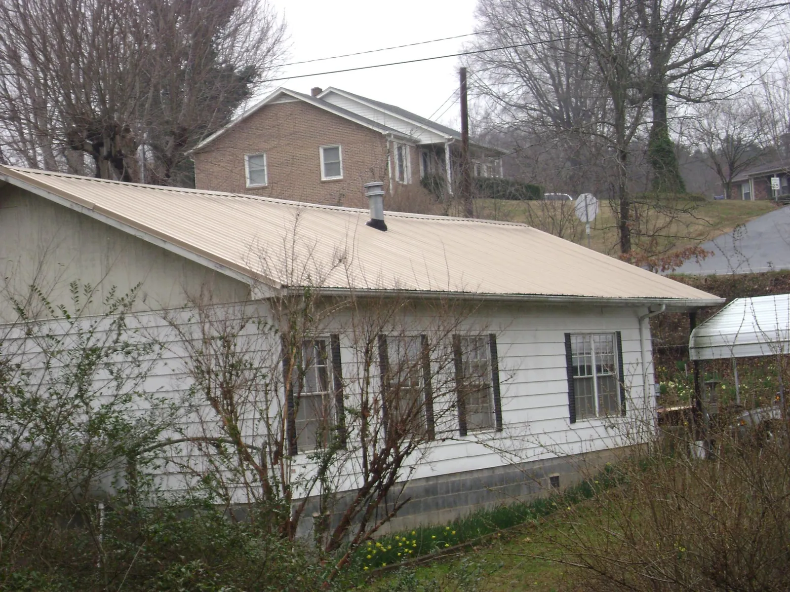 Tan metal roof on a white sided house set into a hillside — Commercial Roofing by Roofing Brothers in Kentwood