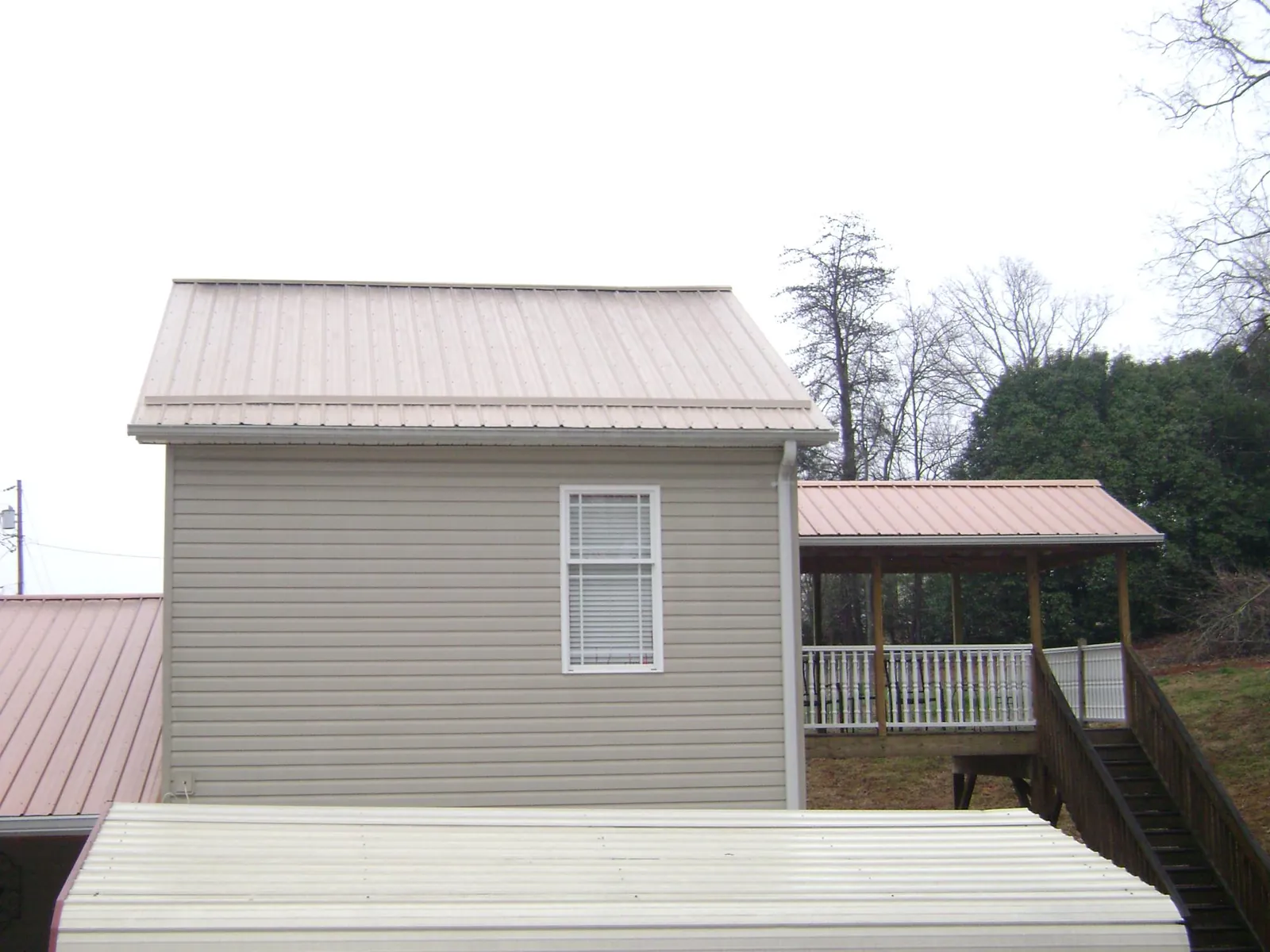 Tan metal roofs on a two story addition and attached porch, from a Roof Replacement job in Kentwood